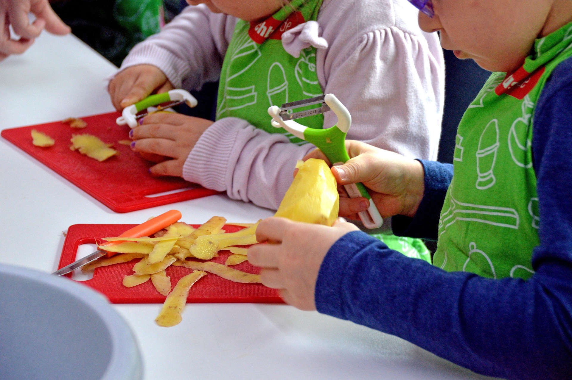 Zwei Kinder mit grüner Schürze schälen Kartoffeln