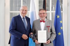 Alfred Sammetinger hält die Urkunde, die er mit dem Bundesverdienstkreuz überreicht bekommen hat. Neben ihm steht der bayerischen Innenminister Joachim Herrmann.