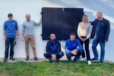 Ein Solarkraftwrek ist an eine weiße Hauswand montiert. Davor stehen die Handwerker, der Stifter der Anlage, sowie die verantwortliche Lehrkraft im Schullandheim Riedenburg und der Geschäftsführer,