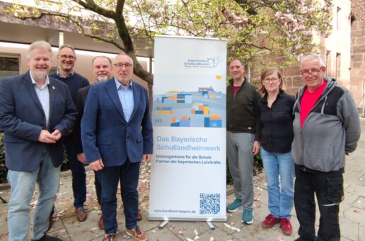 Sechs Männer und eine Frau neben einem Plakat mit dem Logo des Bayerischen Schullandheimwerks.