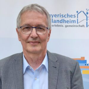 Ein Mann mit Brille vor dem Logo des Bayerischen Schullandheimwerks